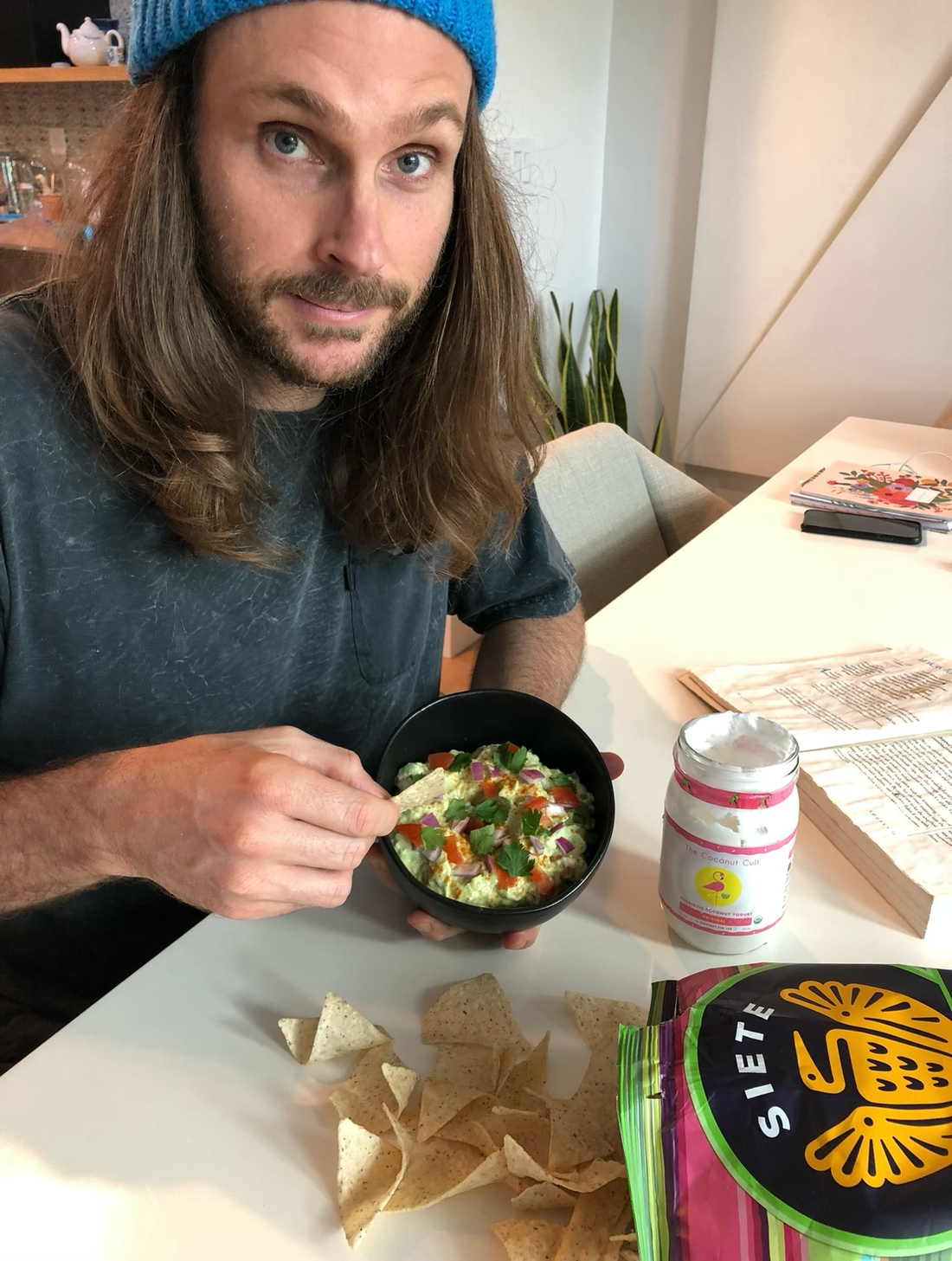 Noah, Coconut Cult founder, in a blue beanie showing a Thanksgiving appetizer with probiotic guacamole and yogurt.