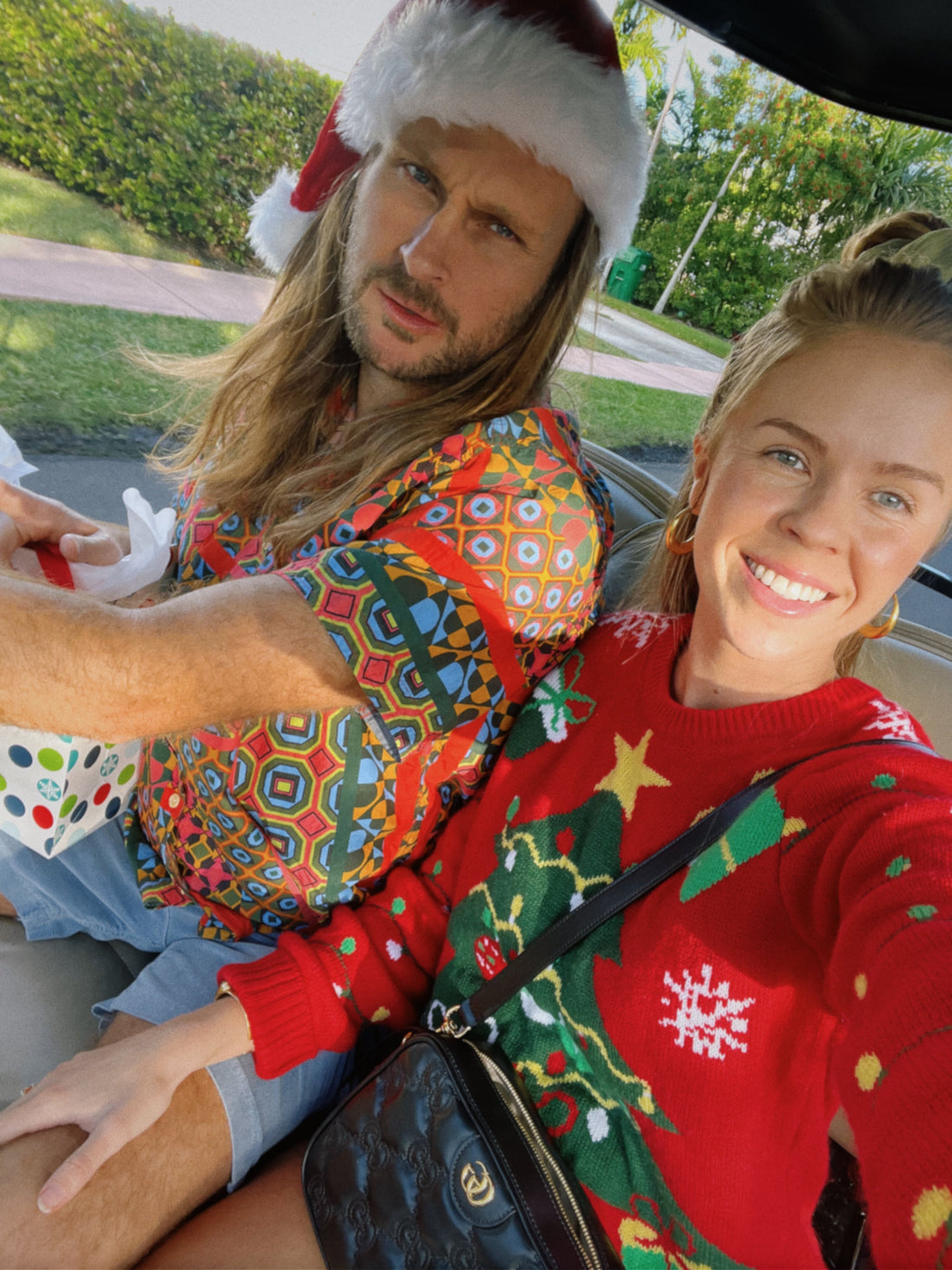 Coconut Cult founder, Noah, in a Santa Claus hat holding a holiday gift and Creative Producer Brittany in a Christmas tree sweater zooming around the neighborhood in a golf cart.